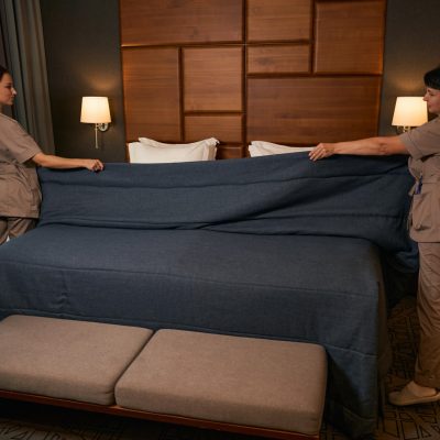 A pair of hotel maids preparing a clean bed that's been treated.